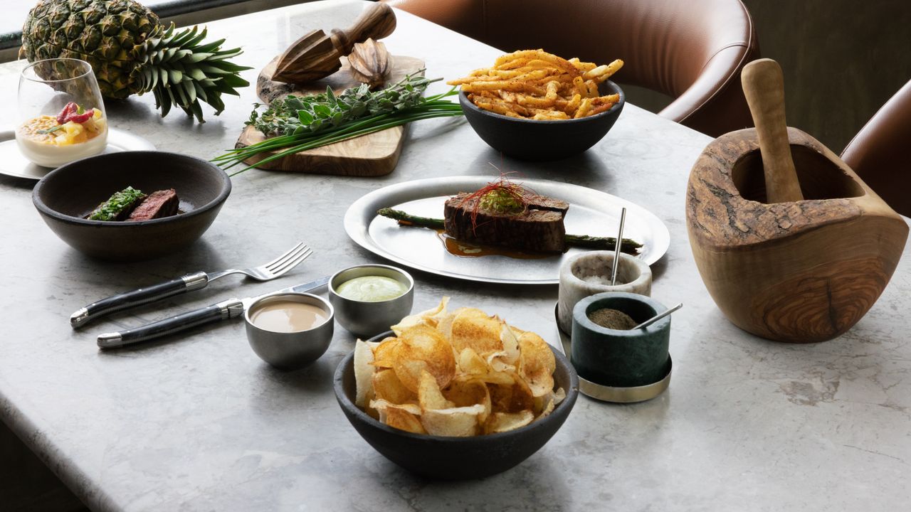 Elegant table setting with gourmet steak, chips, herbs, and sauces, exuding a rustic and sophisticated vibe.