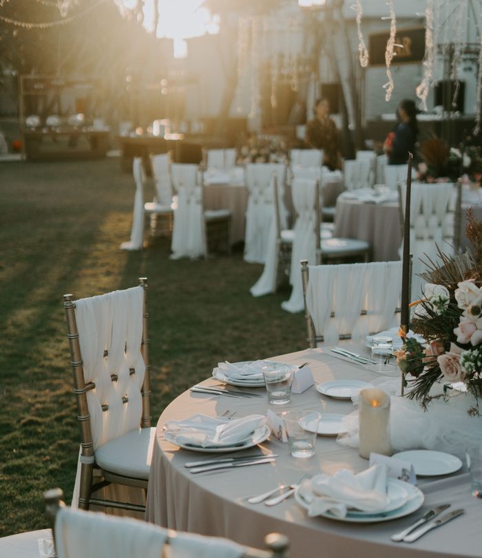 A beautifully arranged outdoor wedding reception with elegantly set tables and chairs at sunset.